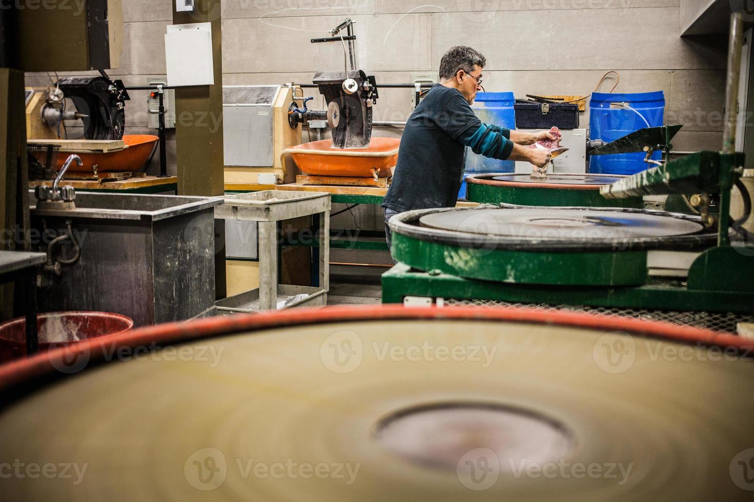 Homme travaillant un vase en verre soufflé sur disque de ponçage en silice photo