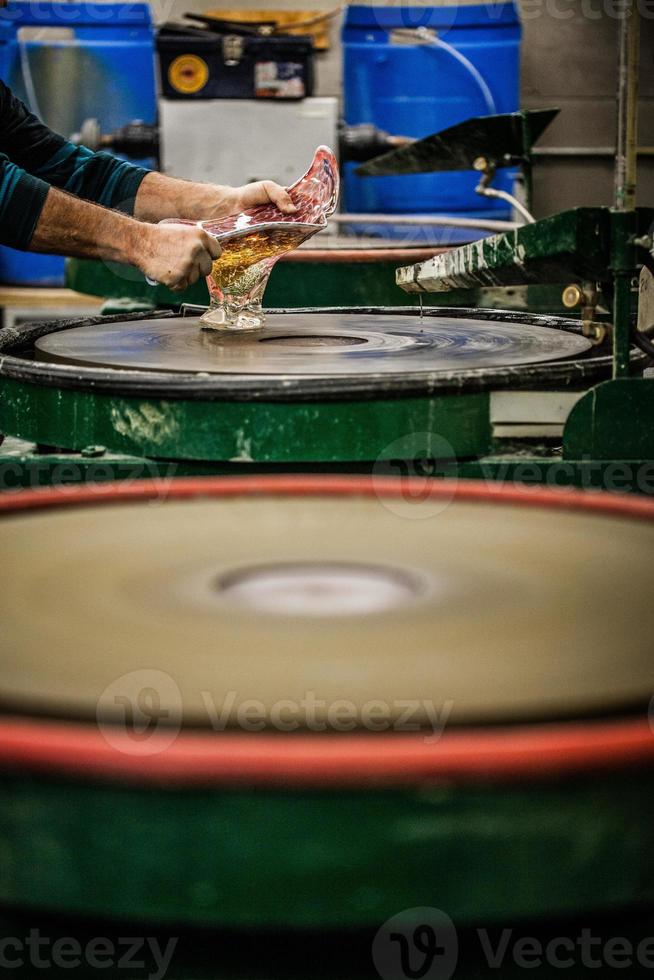 Homme travaillant un vase en verre soufflé sur disque de ponçage en silice photo