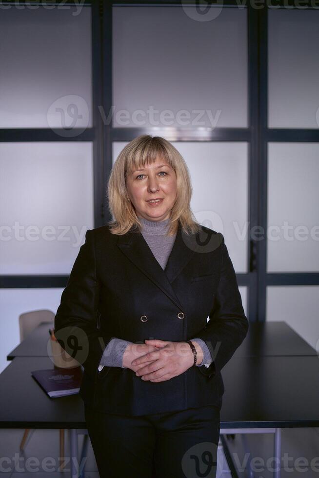 portrait de une blond milieu âge femme dans une affaires costume dans le Bureau photo