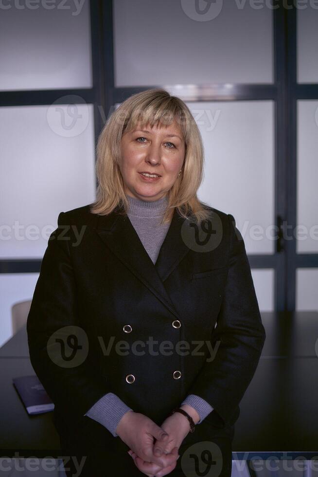 portrait de une blond milieu âge femme dans une affaires costume dans le Bureau photo