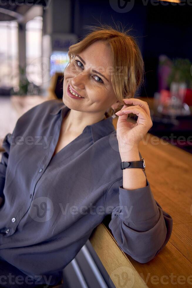 attrayant milieu âge femme dans une bar avec une neutre conception, portant large jambe un pantalon et une soie chemisier photo