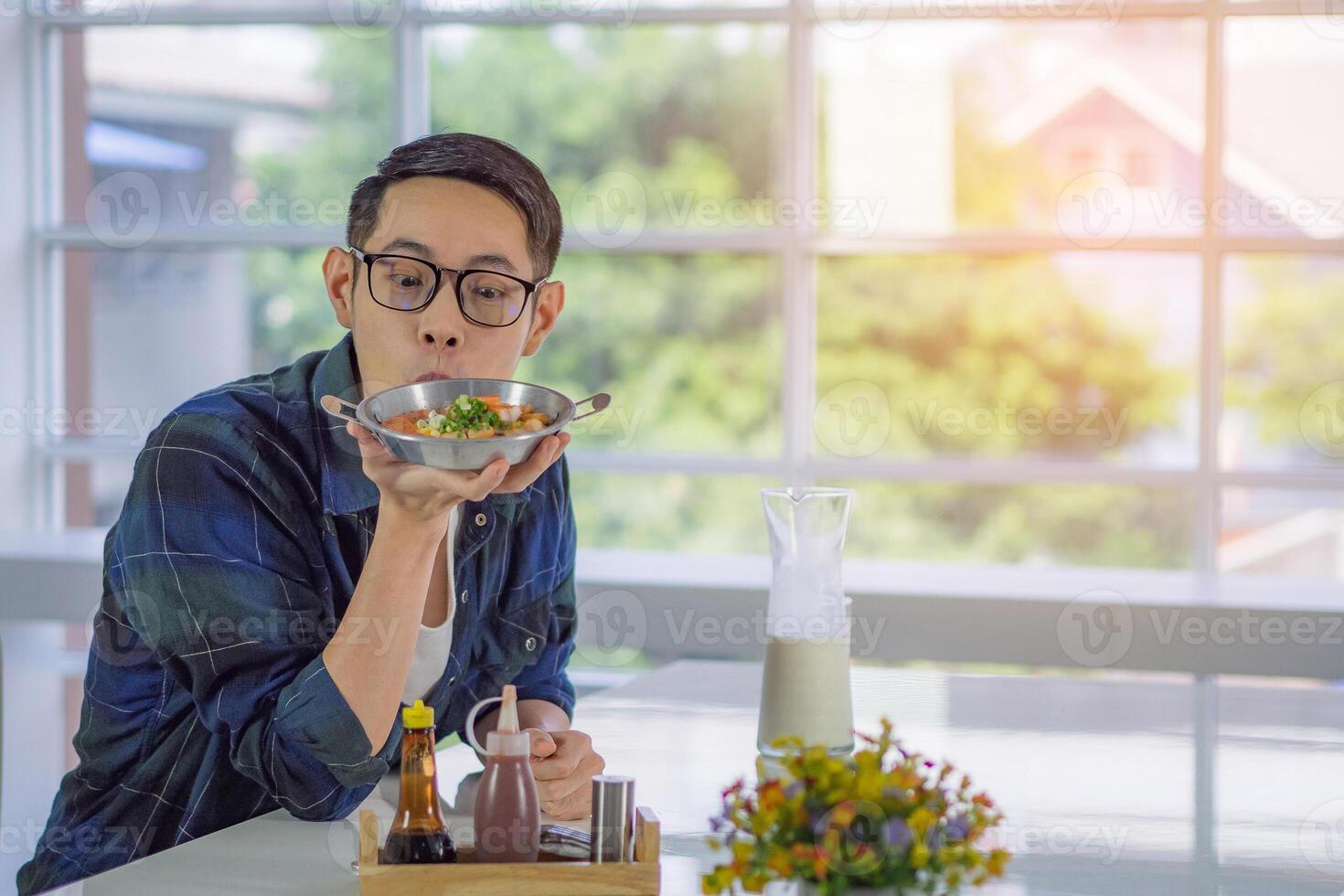 une Jeune homme en portant et à la recherche à le frit Oeuf servi sur une la poêle avec coloré garnitures servi sur une la poêle tandis que séance sur une chaise dans le cuisine chambre. espace pour texte. Facile nourriture pour petit déjeuner photo