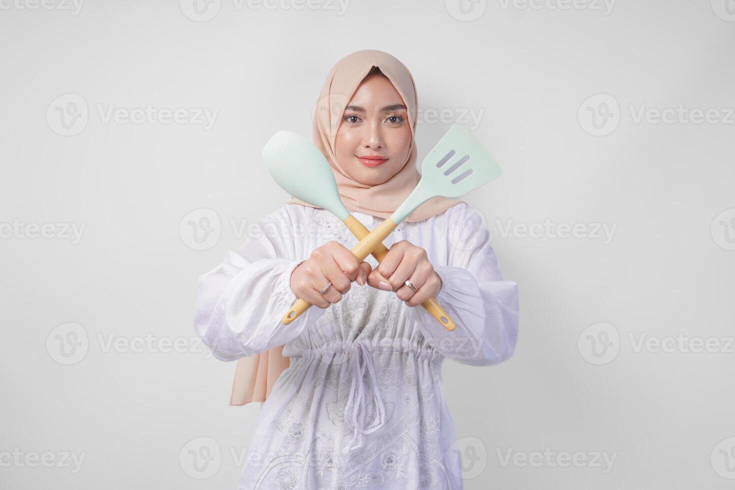 mécontent asiatique femme dans voile hijab Faire une refus ou rejet signe, en disant Non, demander à Arrêtez geste en utilisant spatule et cuisine ustensiles photo