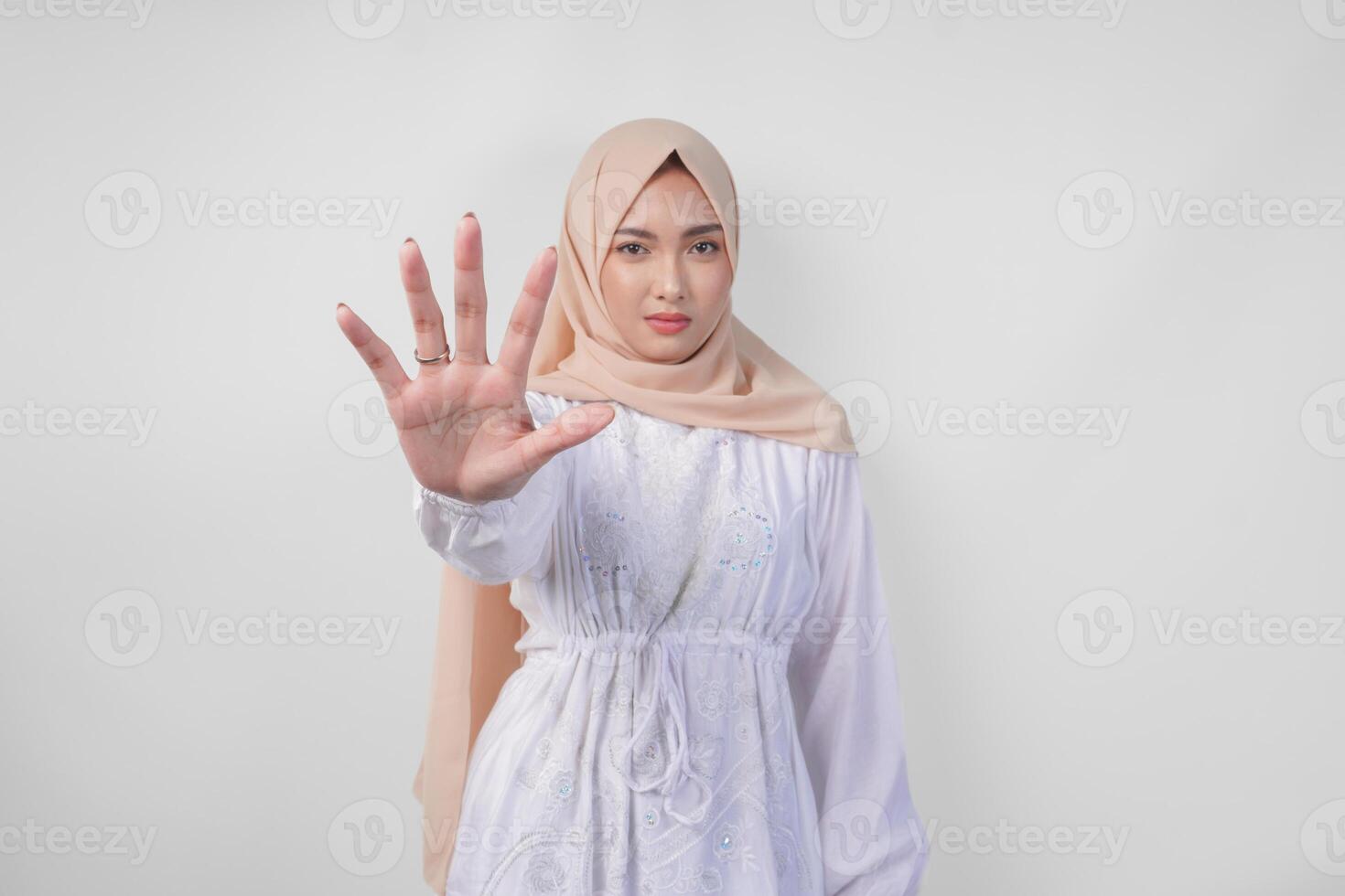 Jeune asiatique musulman femme portant blanc robe et hijab montrant sa paume à faire une Arrêtez geste avec sérieux expression photo