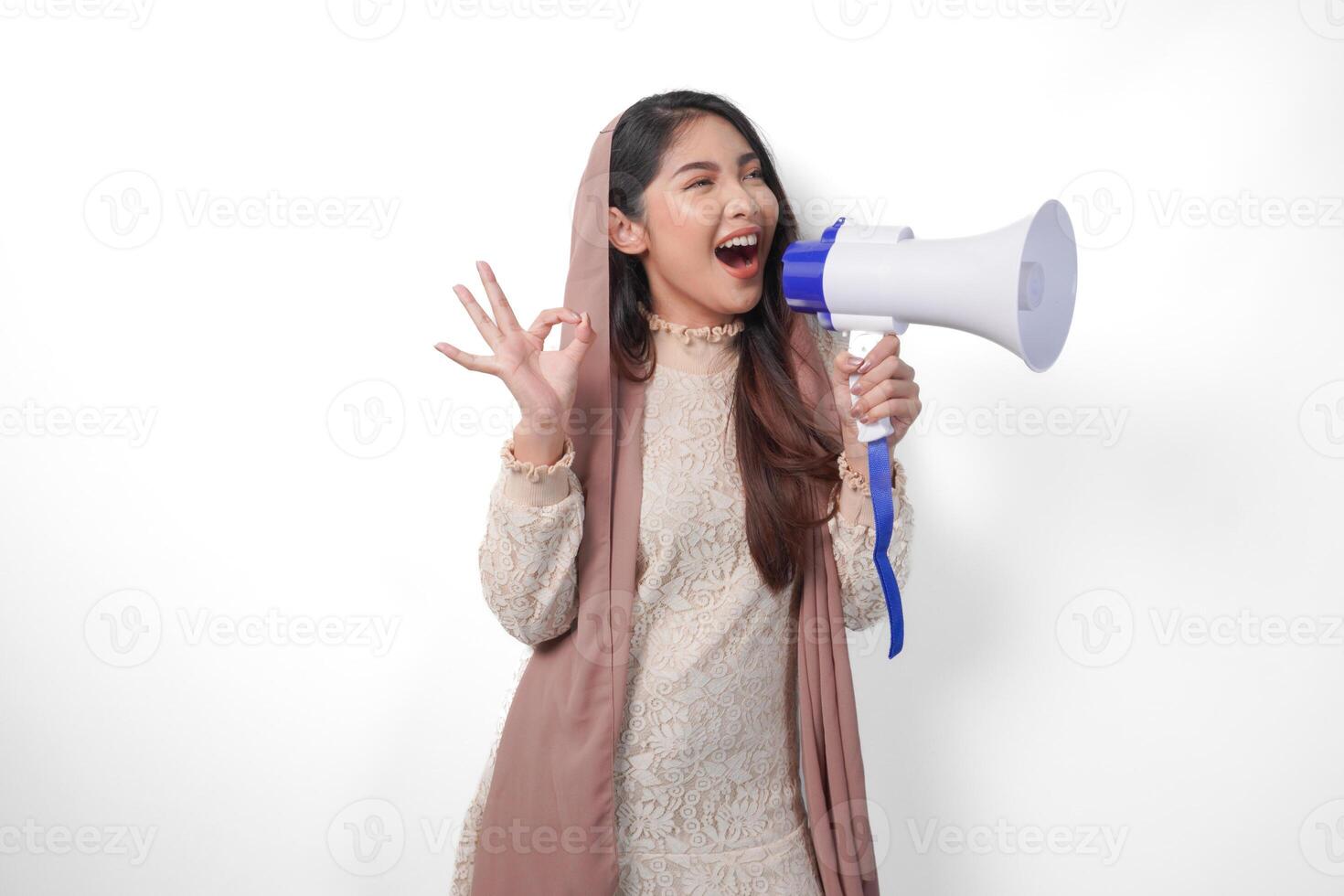 attrayant Jeune asiatique musulman femme dans voile hijab faire des gestes D'accord d'accord, bien signe avec sa les doigts tandis que en criant à mégaphone. Ramadan et eid mubarak concept photo