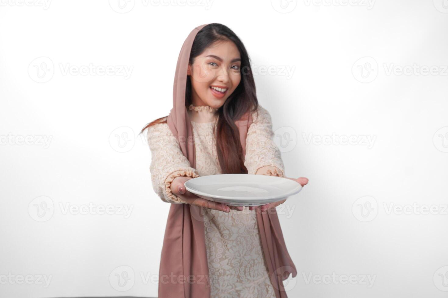 excité asiatique musulman femme en portant assiette et coutellerie à manger après jeûne tandis que souriant gaiement sur isolé blanc Contexte. Ramadan concept photo