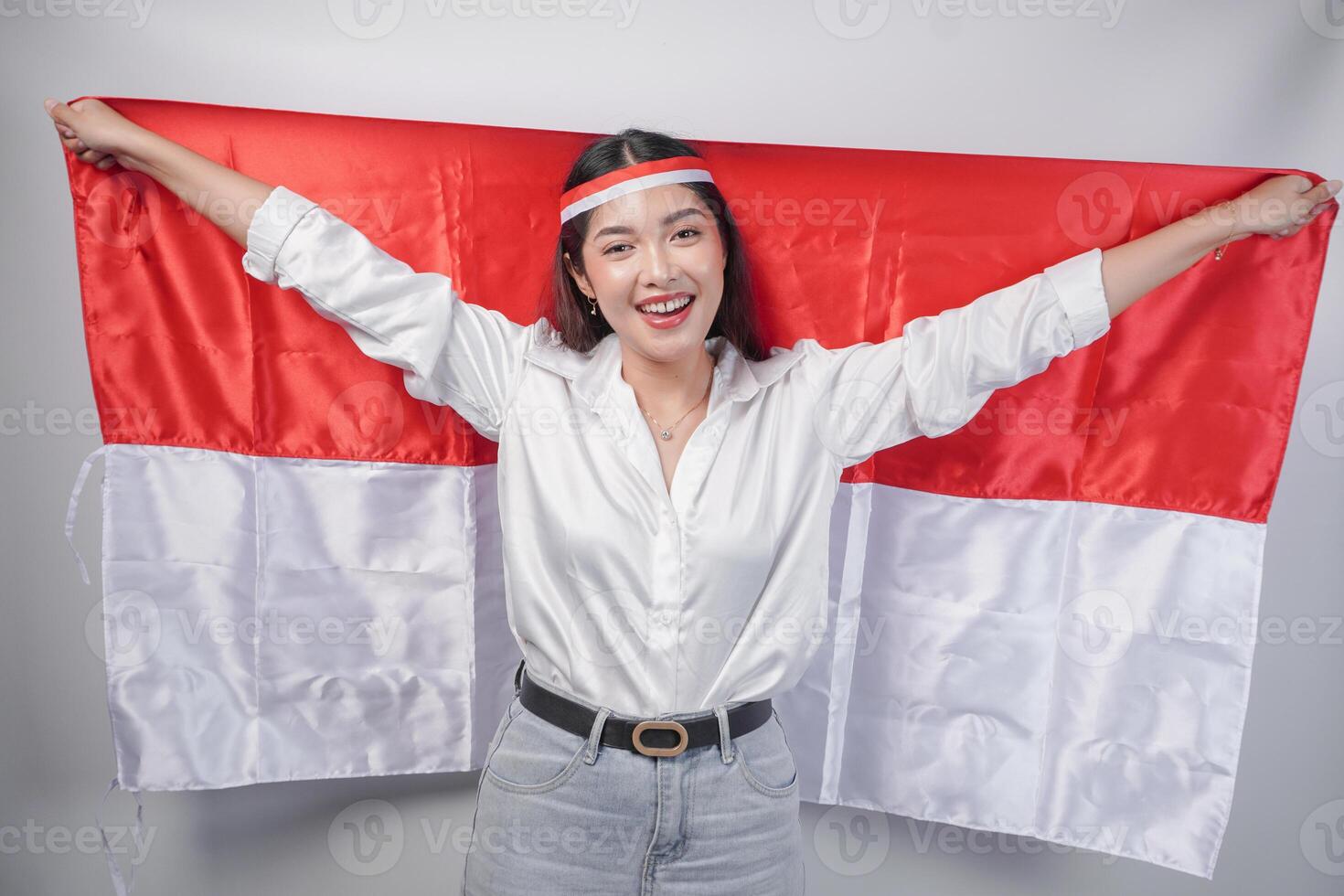 souriant asiatique femme portant drapeau Bandeau et décontractée tenue tandis que en portant Indonésie drapeau à le dos. indépendance journée publicité concept photo