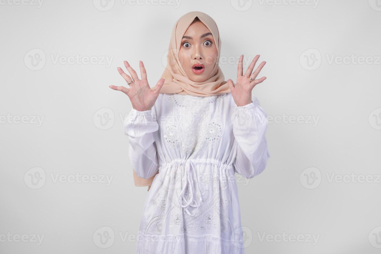 portrait de Jeune asiatique musulman femme portant blanc robe et hijab avec surpris expression et bouche large ouvert après audition choquant nouvelles plus de isolé blanc Contexte photo