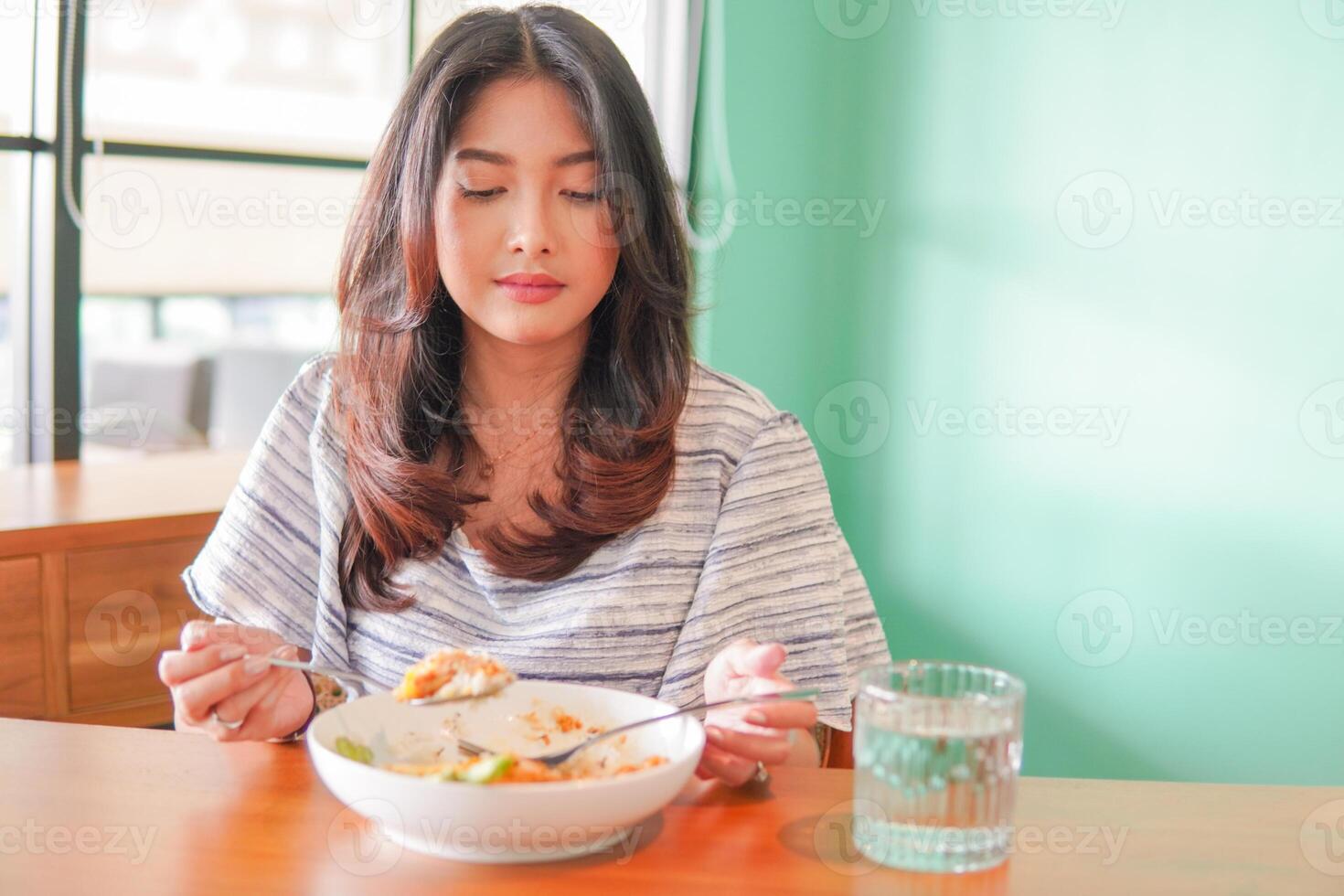 portrait de un excité Jeune asiatique femme portant robe séance à une restaurant, en mangeant et profiter petit déjeuner avec une de bonne humeur sourire photo