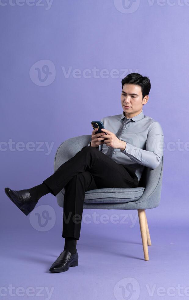 portrait de asiatique affaires homme séance sur canapé, isolé sur violet Contexte photo