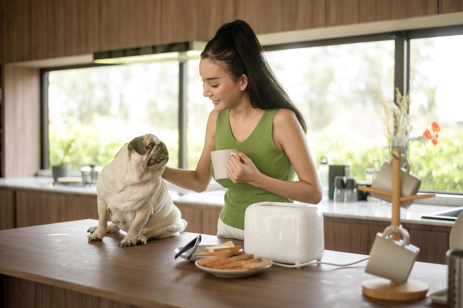 asiatique femme en train de préparer café et pain grillé pain pour petit déjeuner prendre plaisir avec chien à le cuisine table dans le Matin photo