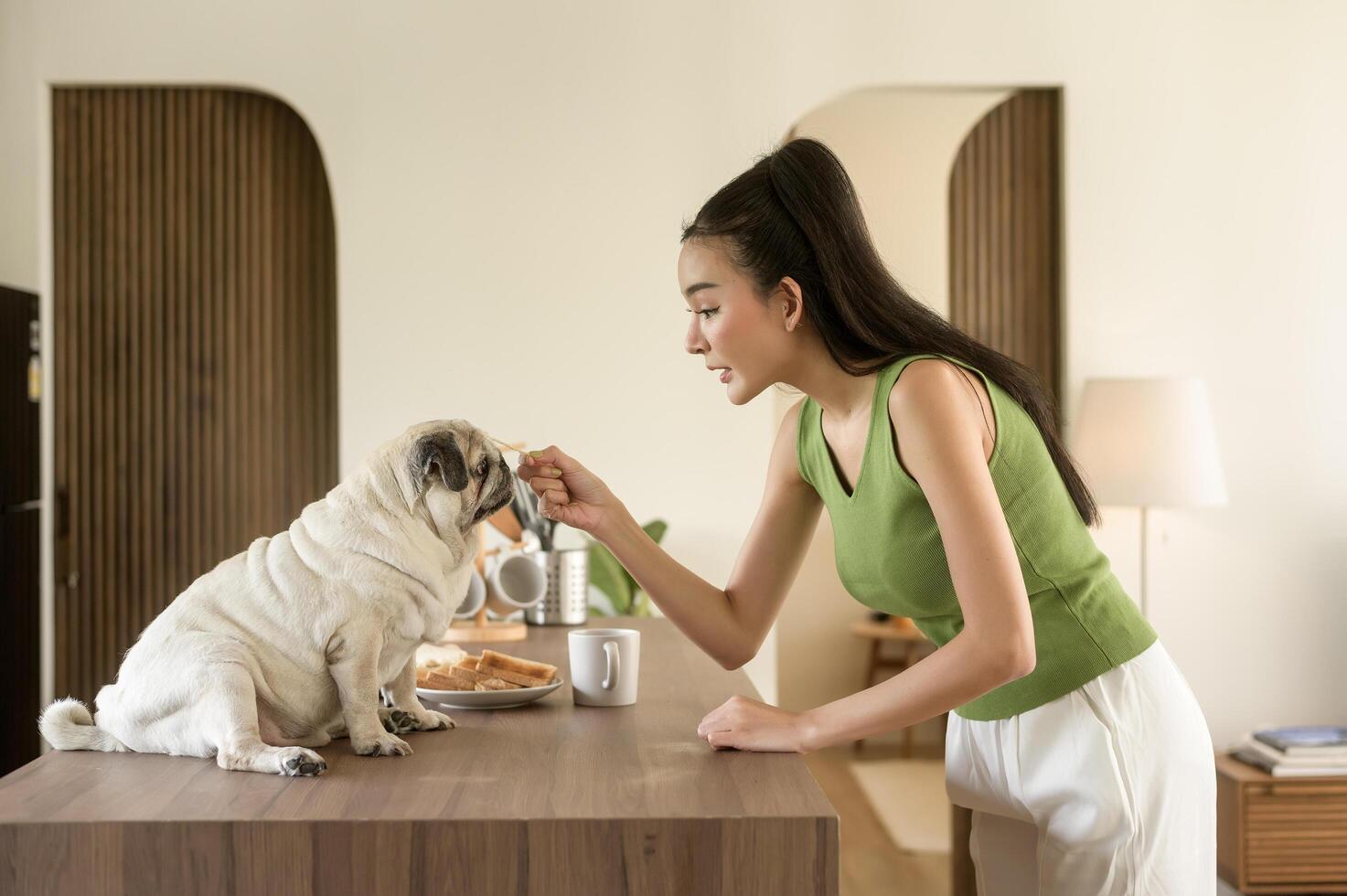 asiatique femme en train de préparer café et pain grillé pain pour petit déjeuner prendre plaisir avec chien à le cuisine table dans le Matin photo