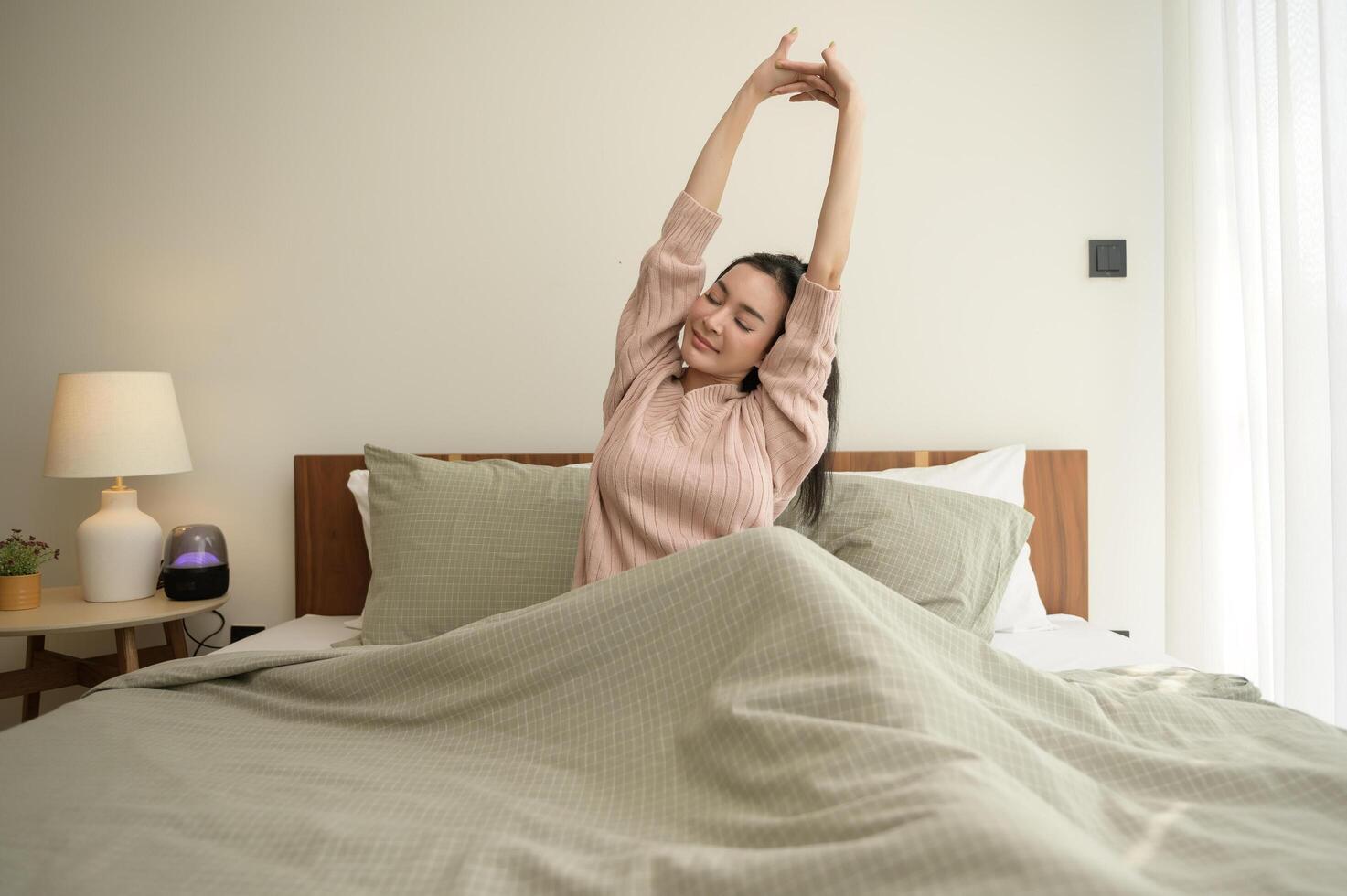 Jeune asiatique femme élongation dans lit après veille en haut dans le Matin photo