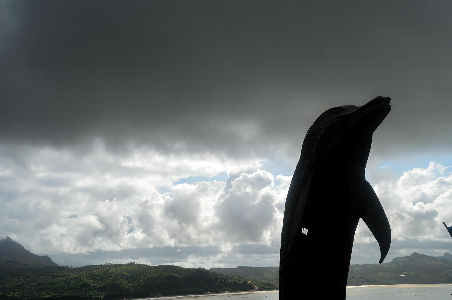 silhouette de une dauphin statue contre une Contexte de bord de mer collines avec nuageux temps photo