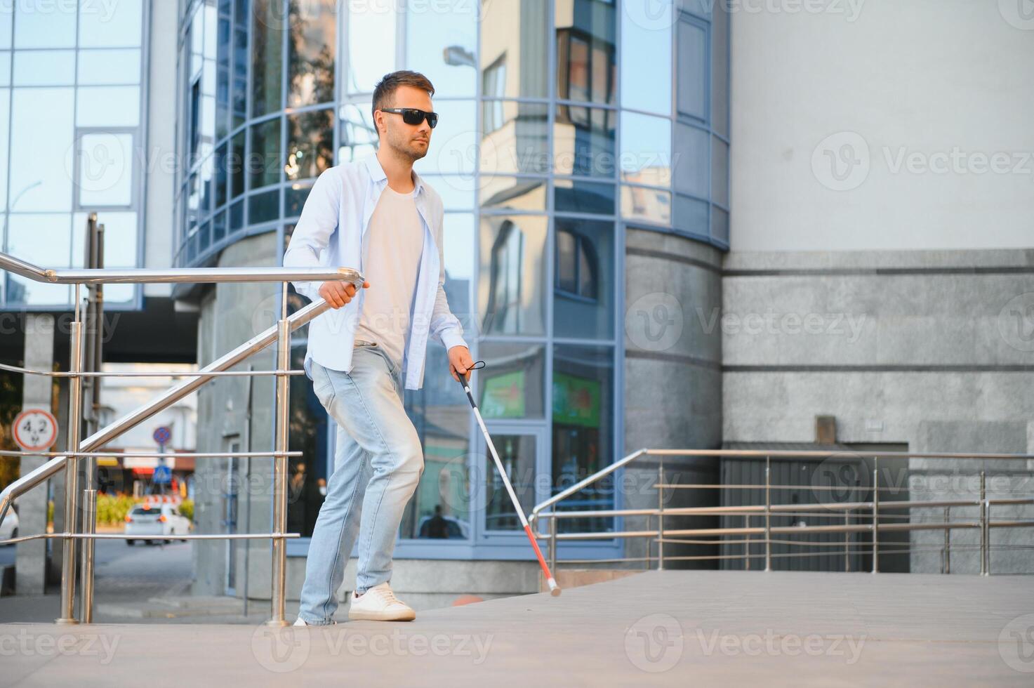 Jeune Beau aveugle homme en marchant avec bâton dans ville photo