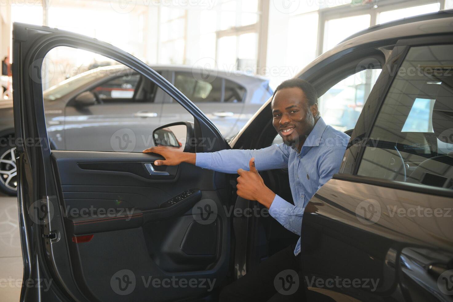 voiture propriétaire. joyeux afro gars souriant, séance dans Nouveau voiture conduite de concession magasin photo