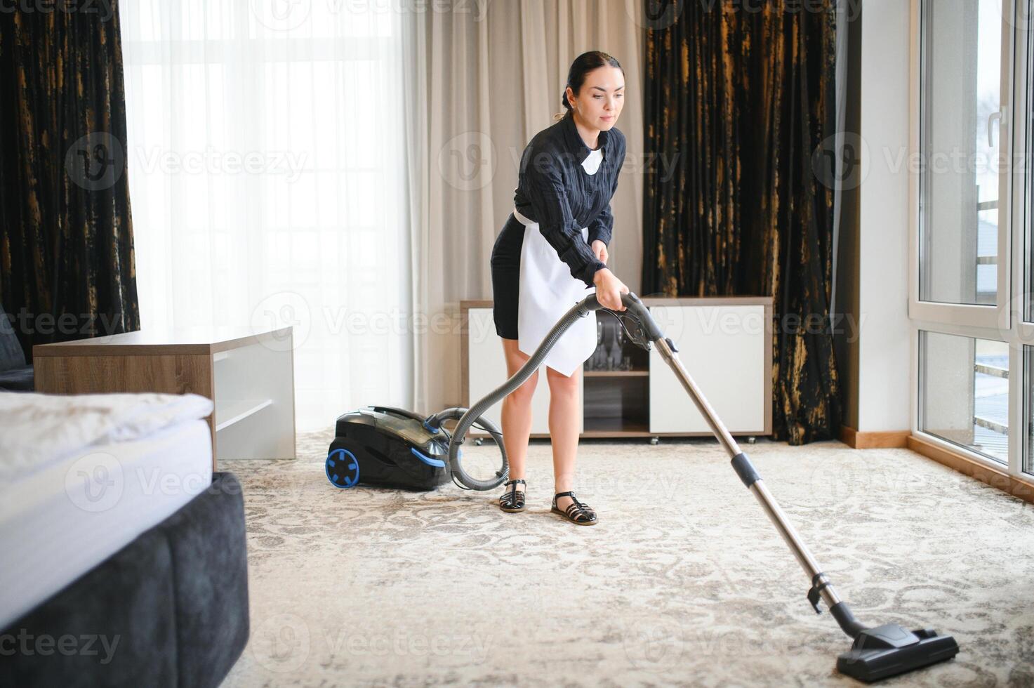 Jeune gouvernante nettoyage tapis avec vide nettoyeur dans Hôtel pièce photo