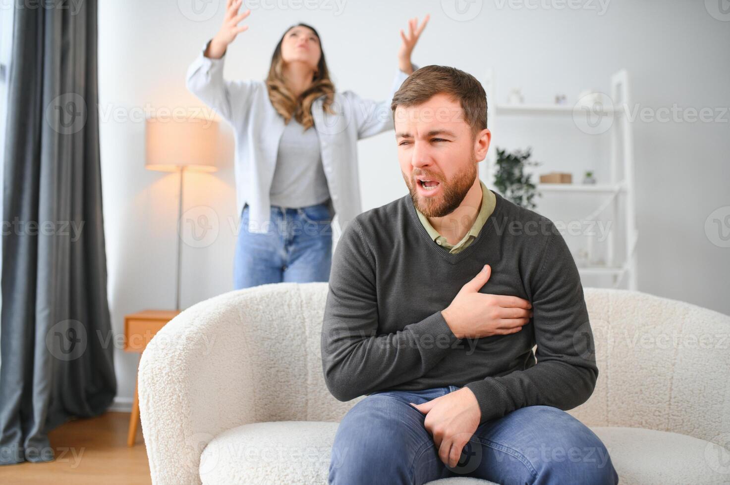 couple argumentant. épouse en criant à sa désespéré mari séance sur une canapé dans le vivant pièce à Accueil photo