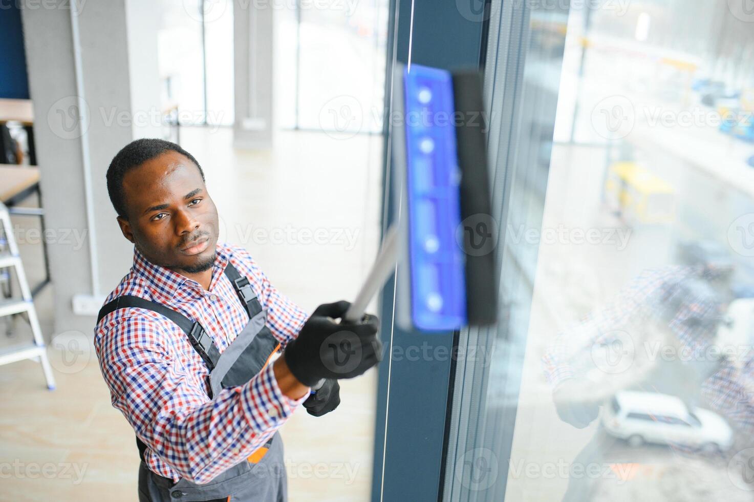 africain Masculin professionnel nettoyage un service ouvrier dans salopette nettoie le les fenêtres et magasin les fenêtres de une boutique avec spécial équipement photo