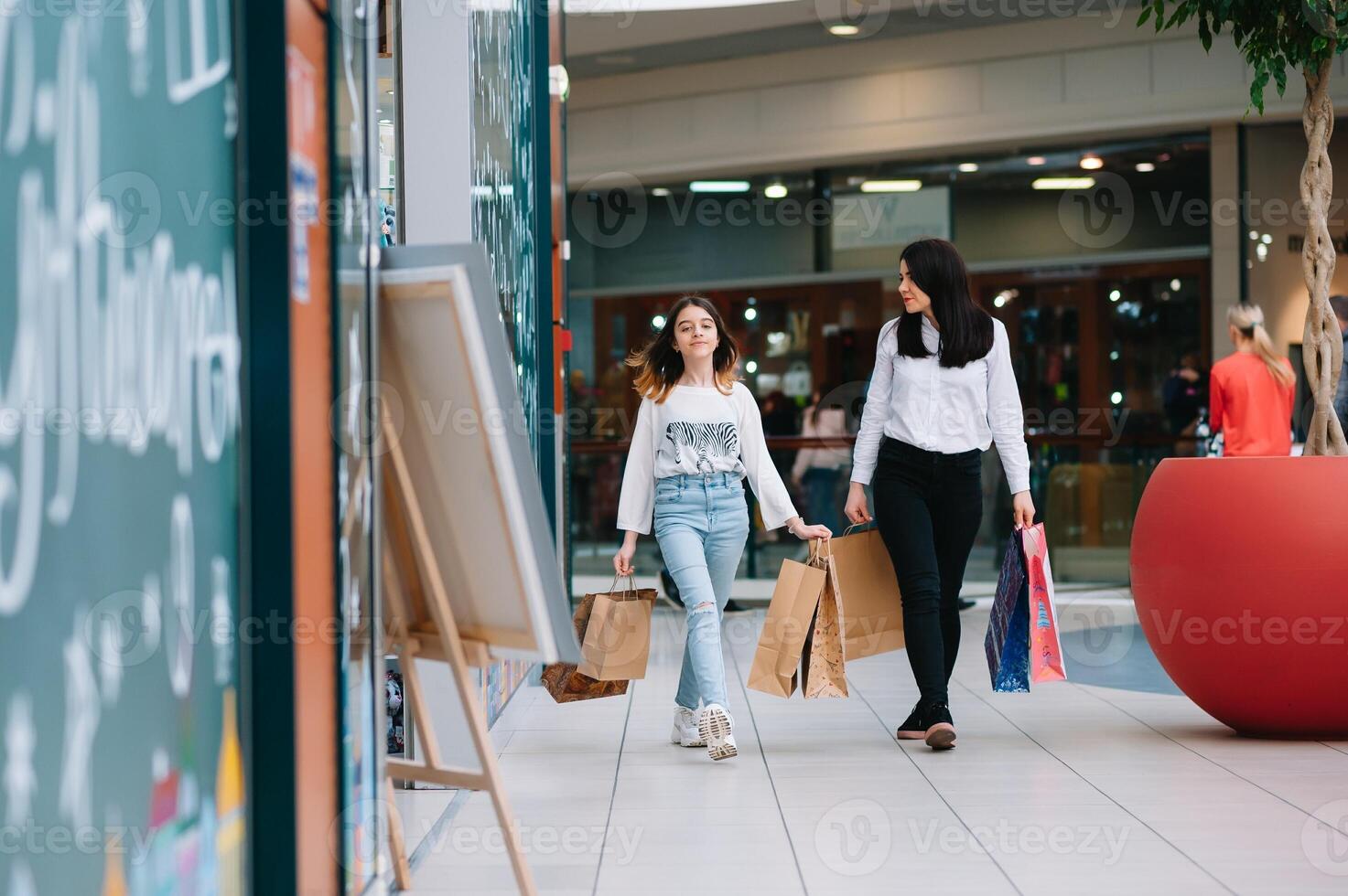 magnifique Jeune maman et adolescent fille sont en portant achats Sacs et souriant tandis que Faire achats dans centre commercial. famille achats photo