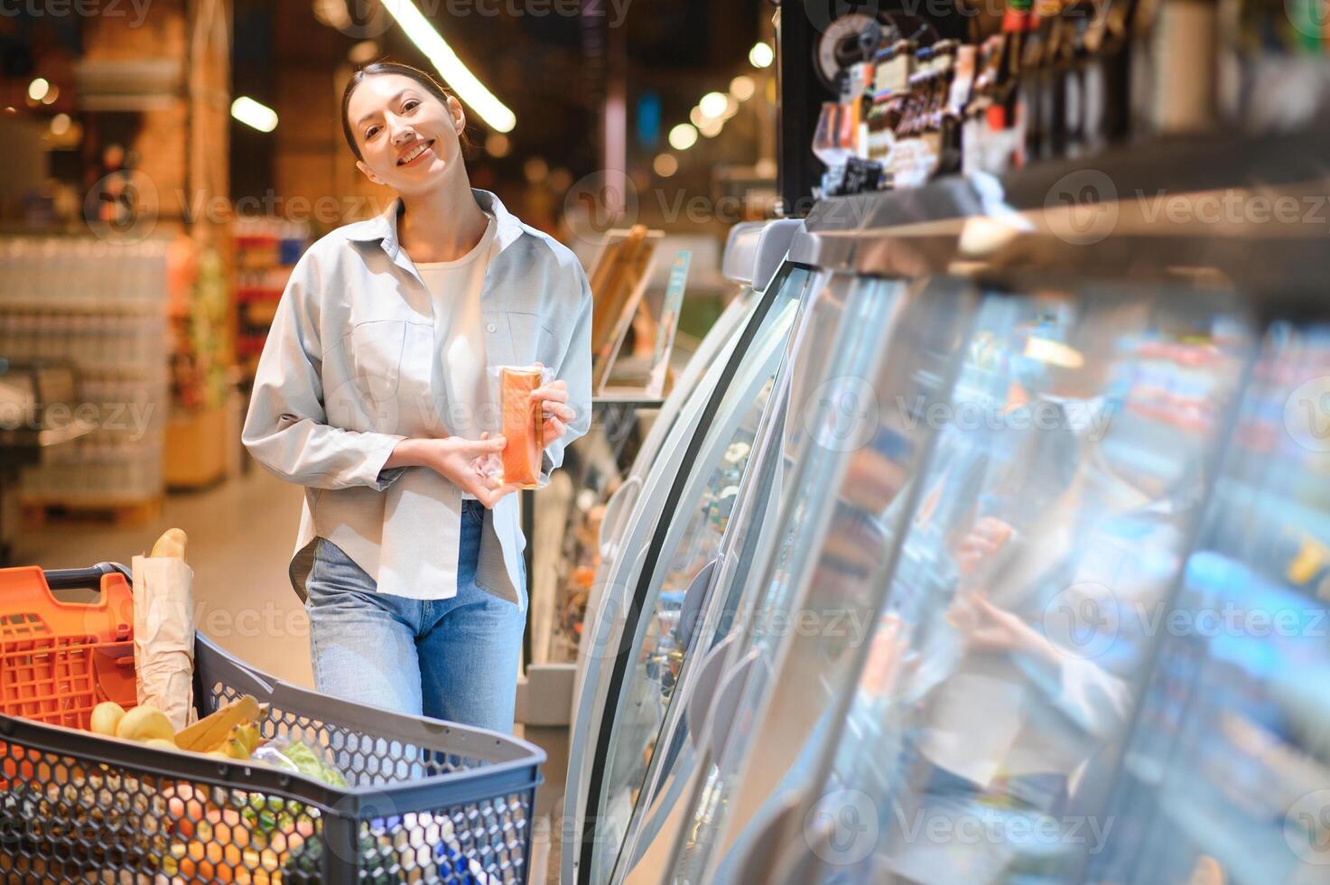 Jeune femme avec une achats sac comme une client achat poisson à le réfrigéré étagère dans le supermarché photo