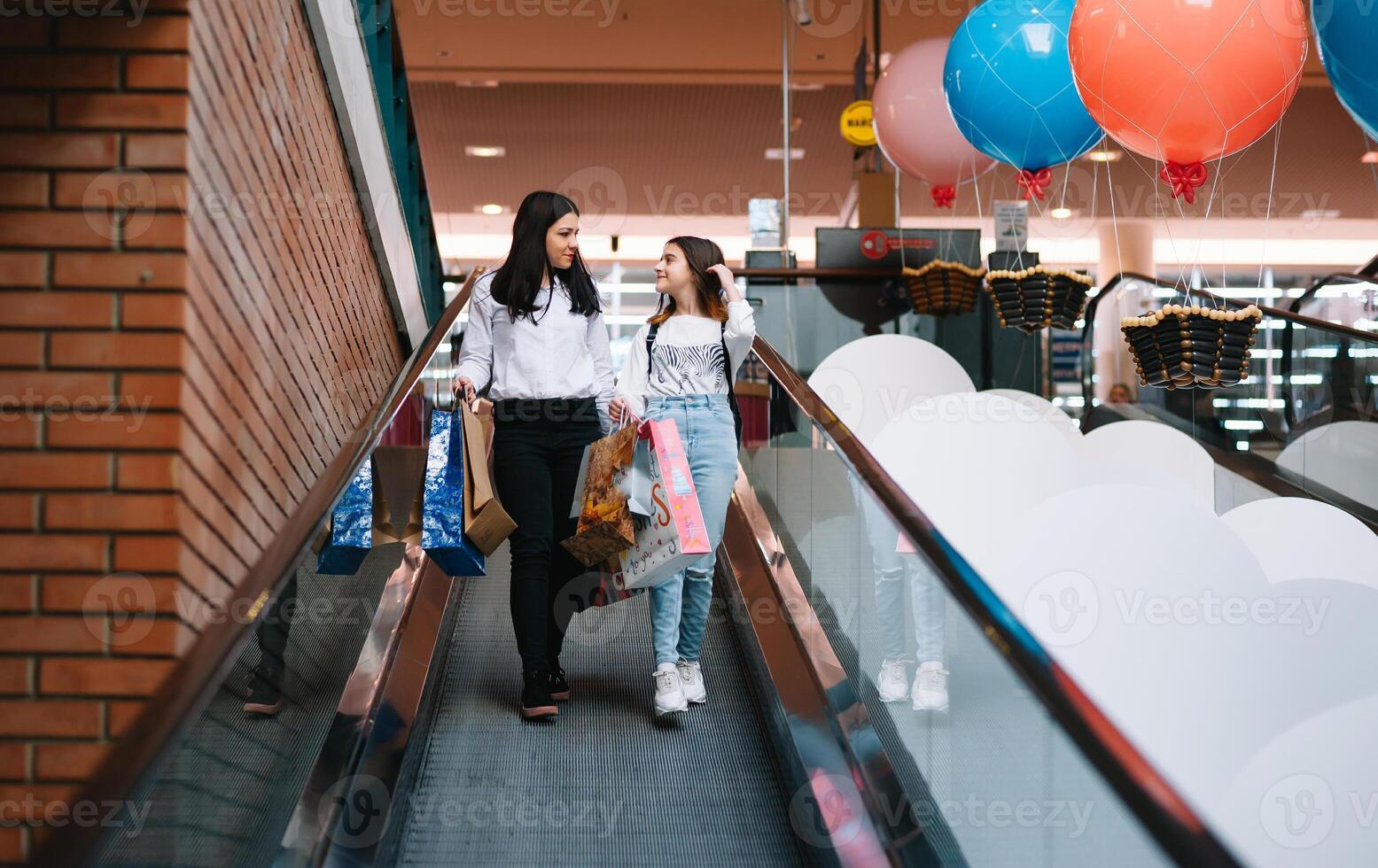 magnifique Jeune maman et adolescent fille sont en portant achats Sacs et souriant tandis que Faire achats dans centre commercial. famille achats photo