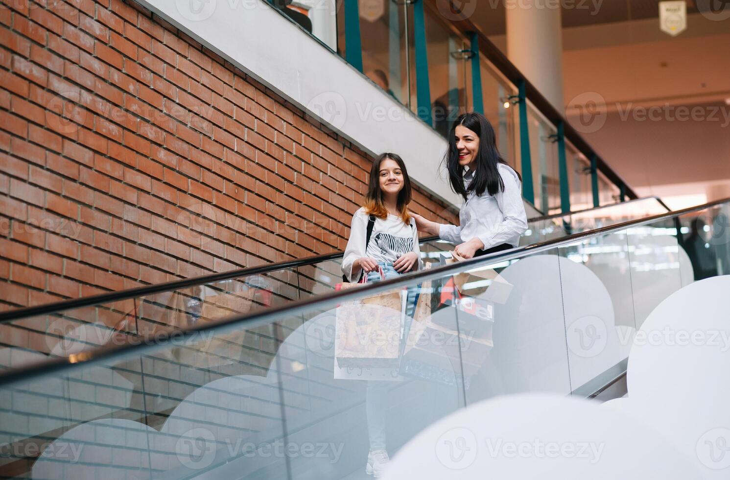 magnifique Jeune maman et adolescent fille sont en portant achats Sacs et souriant tandis que Faire achats dans centre commercial. famille achats photo