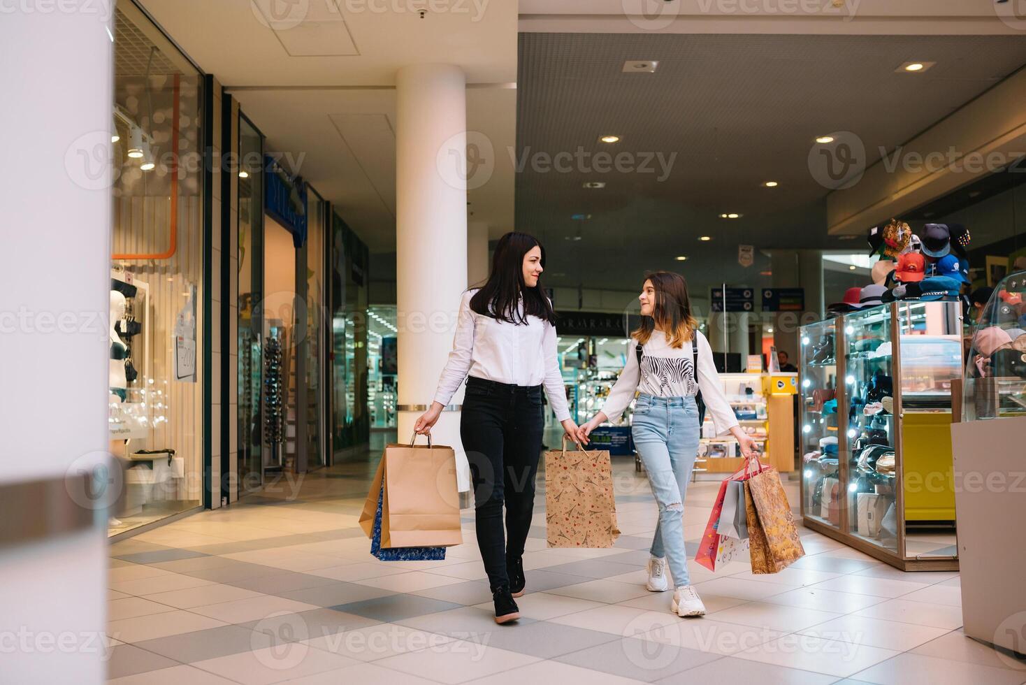 magnifique Jeune maman et adolescent fille sont en portant achats Sacs et souriant tandis que Faire achats dans centre commercial. famille achats photo