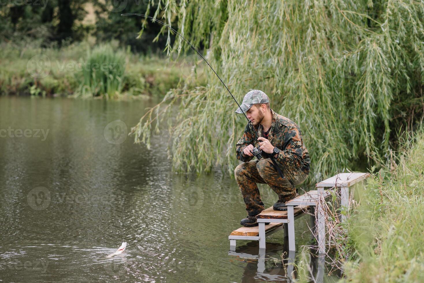 pêche dans rivière.a pêcheur avec une pêche barre sur le rivière banque. homme pêcheur captures une poisson pêche au brochet, filage bobine, poisson, breg rivières. - le concept de une rural partir. article à propos pêche photo