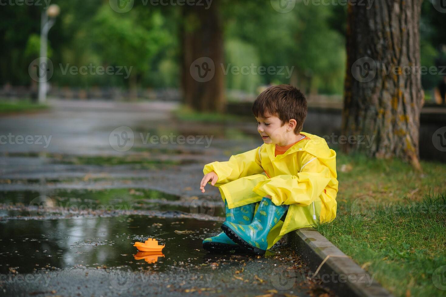 enfant en jouant avec jouet bateau dans flaque. enfant jouer Extérieur par pluie. tomber pluvieux temps en plein air activité pour Jeune les enfants. enfant sauter dans boueux flaques d'eau. imperméable veste et bottes pour bébé. enfance photo