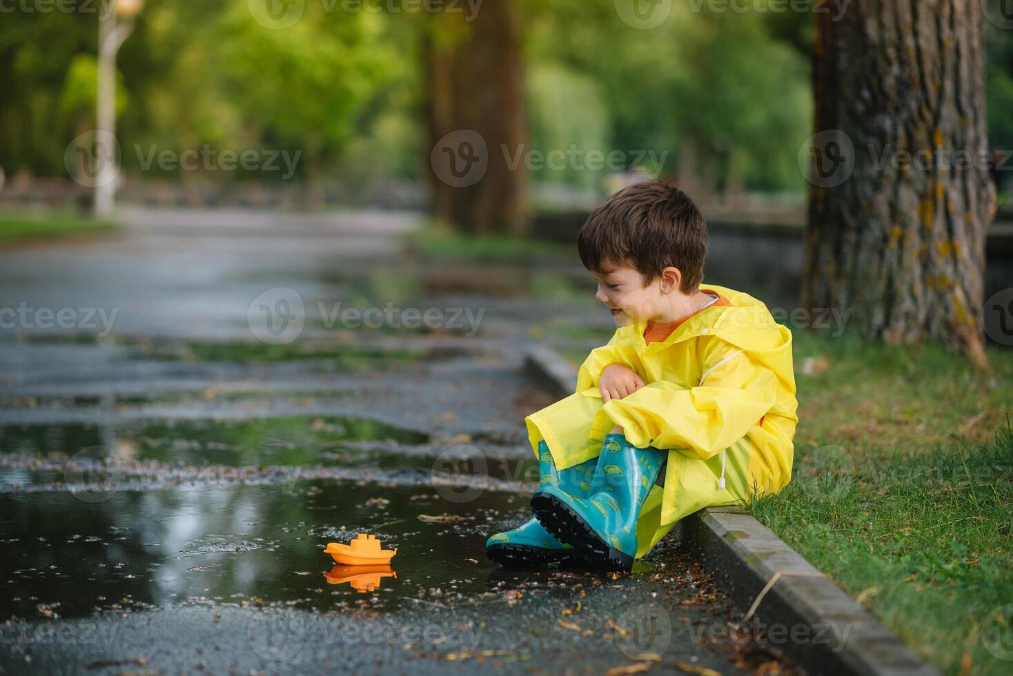 enfant en jouant avec jouet bateau dans flaque. enfant jouer Extérieur par pluie. tomber pluvieux temps en plein air activité pour Jeune les enfants. enfant sauter dans boueux flaques d'eau. imperméable veste et bottes pour bébé. enfance photo