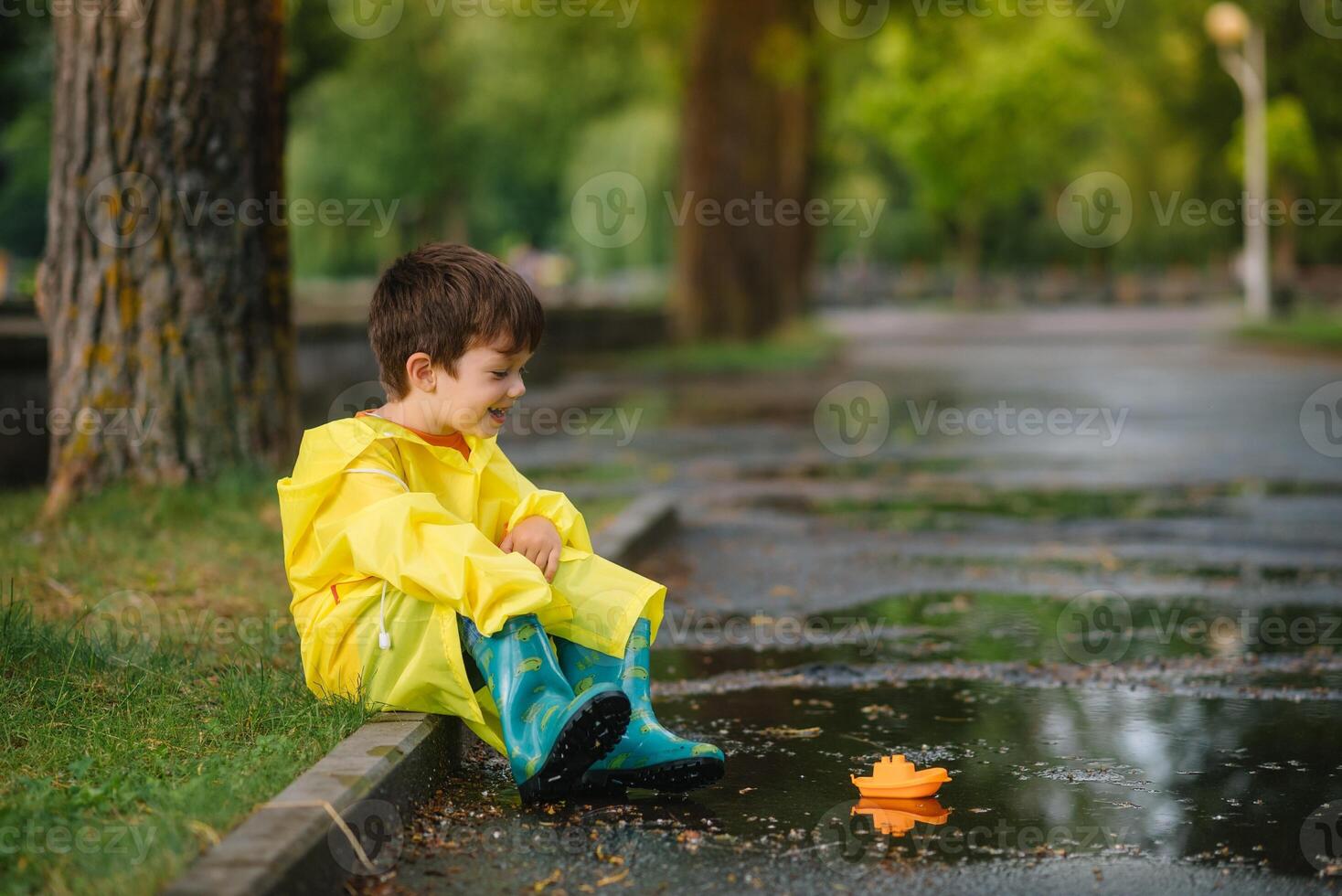 enfant en jouant avec jouet bateau dans flaque. enfant jouer Extérieur par pluie. tomber pluvieux temps en plein air activité pour Jeune les enfants. enfant sauter dans boueux flaques d'eau. imperméable veste et bottes pour bébé. enfance photo