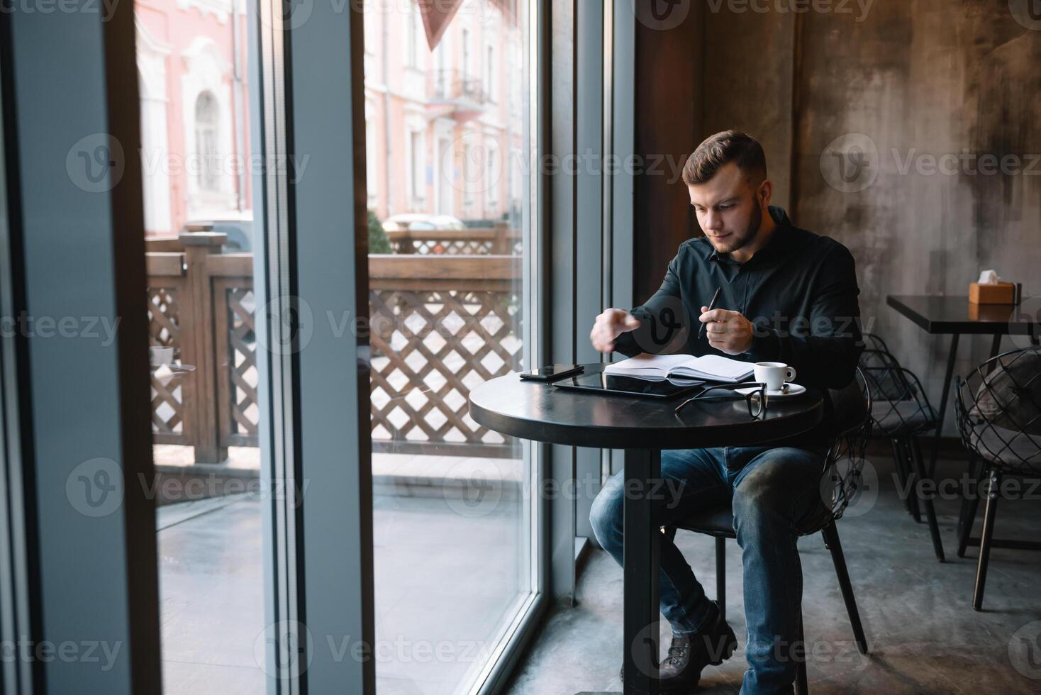Beau homme d'affaire en utilisant une numérique tablette et en buvant café tandis que séance dans café dans le ville centre. photo
