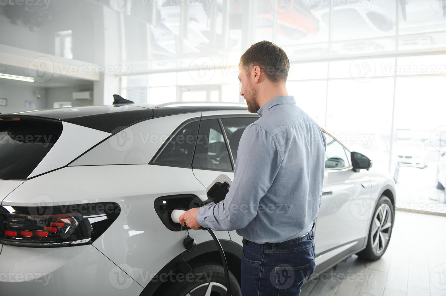 barbe homme en essayant une Nouveau mise en charge câble avec une voiture mise en charge station à le moteur concession. concept de achat électrique véhicule. intelligent écologique vivant photo