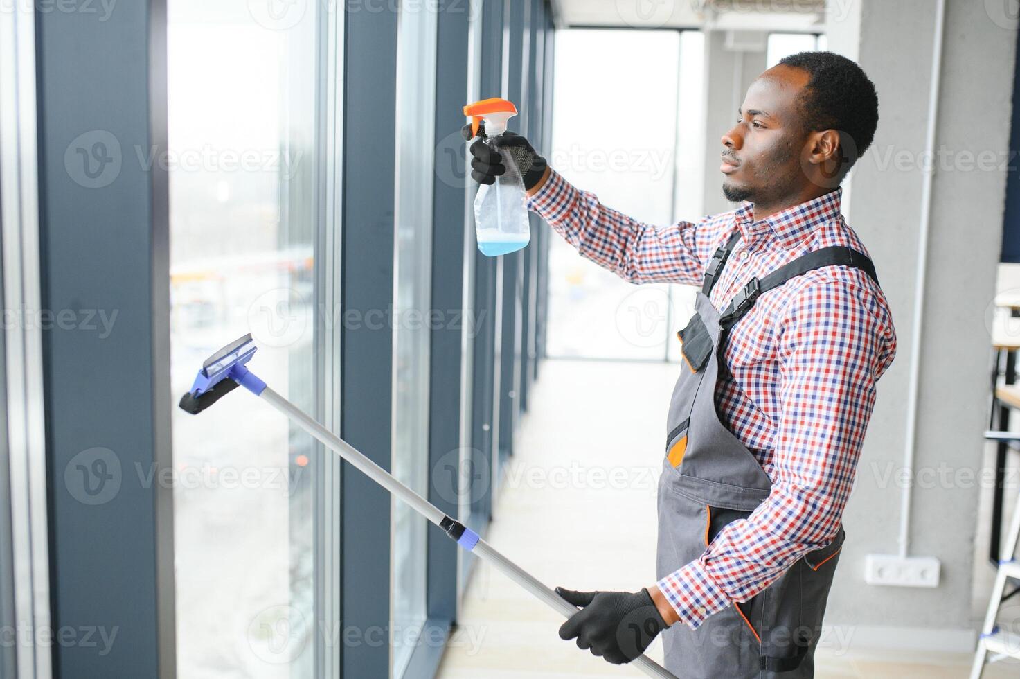 africain Masculin professionnel nettoyage un service ouvrier dans salopette nettoie le les fenêtres et magasin les fenêtres de une boutique avec spécial équipement photo