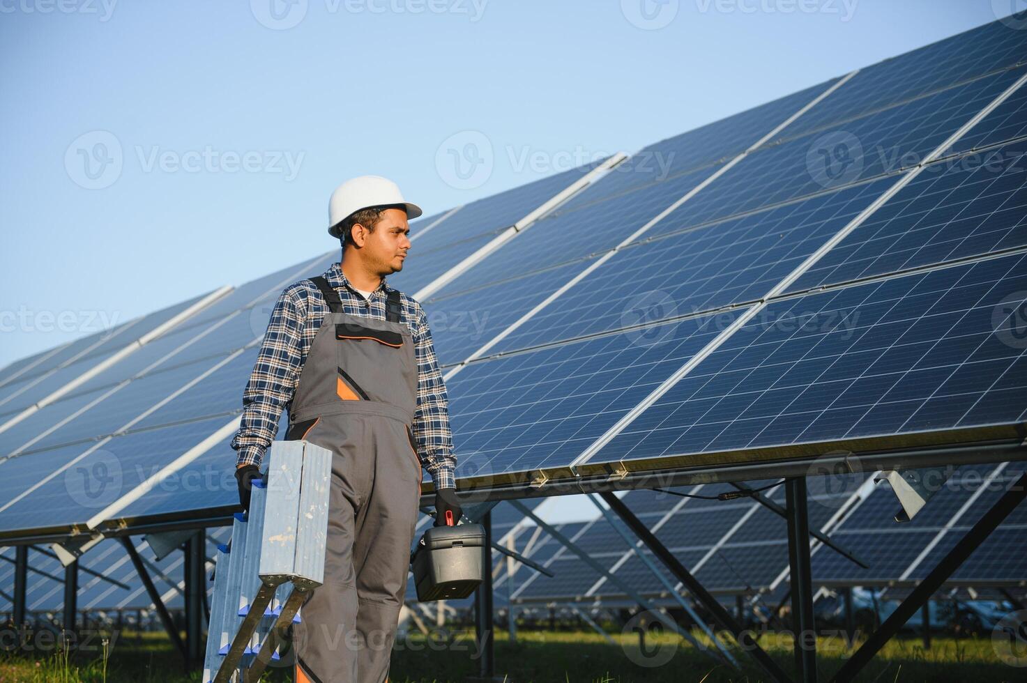 portrait de Jeune Indien homme technicien portant blanc difficile chapeau permanent près solaire panneaux contre bleu ciel. industriel ouvrier solaire système installation photo