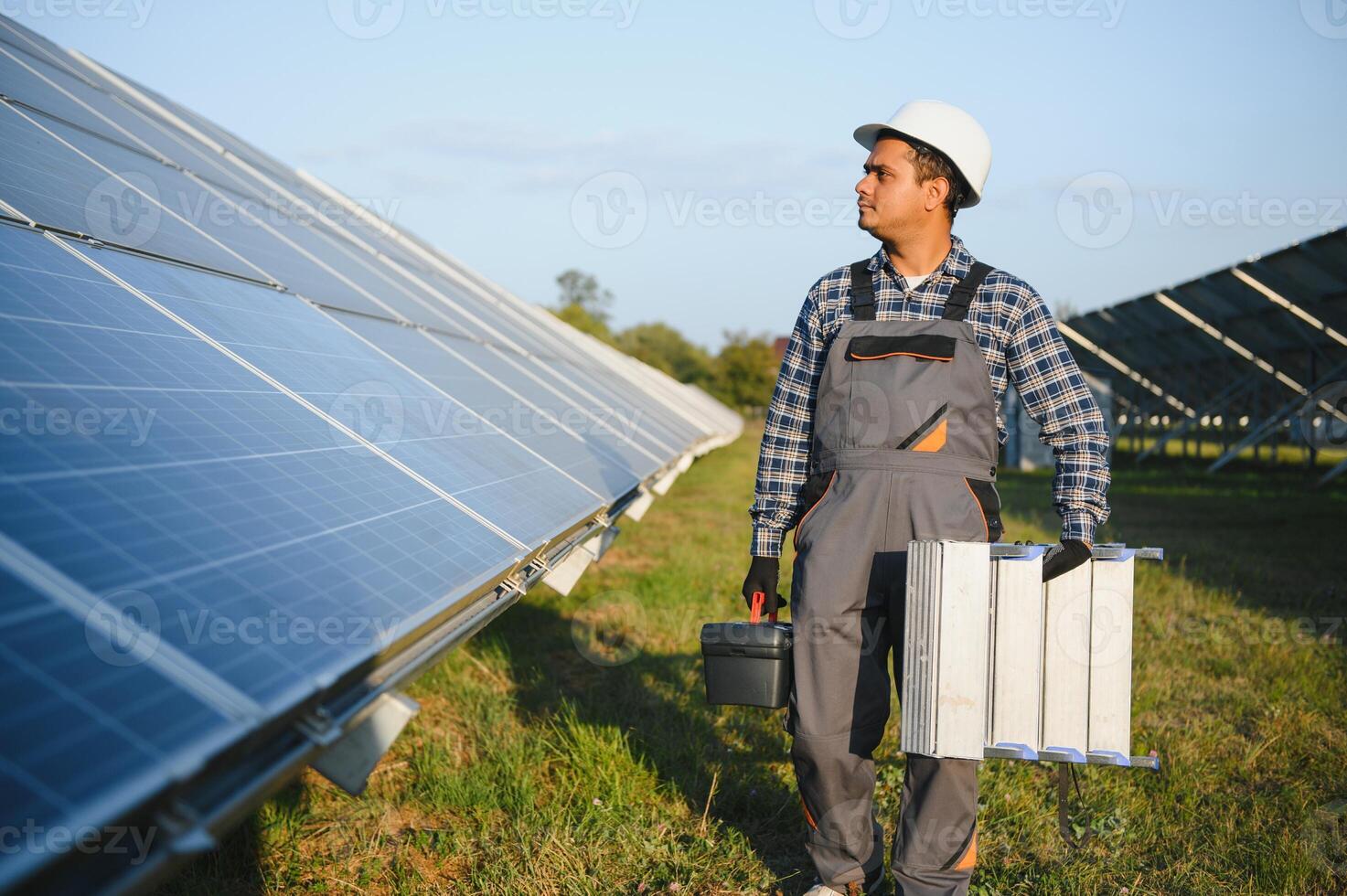 portrait de Jeune Indien homme technicien portant blanc difficile chapeau permanent près solaire panneaux contre bleu ciel. industriel ouvrier solaire système installation photo