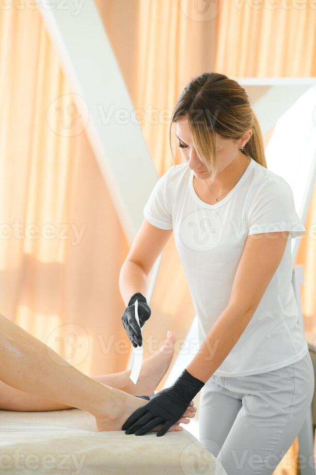 esthéticien fait du épilation Jeune femme sur sa pieds avec la cire, liquide sucre photo