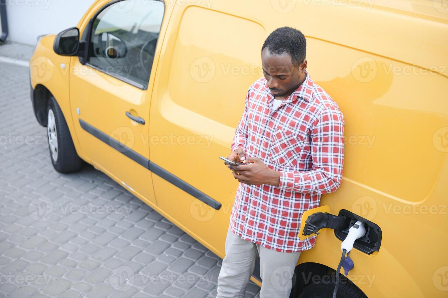 une africain américain homme des stands suivant à Jaune électrique livraison van à électrique véhicule mise en charge stations photo