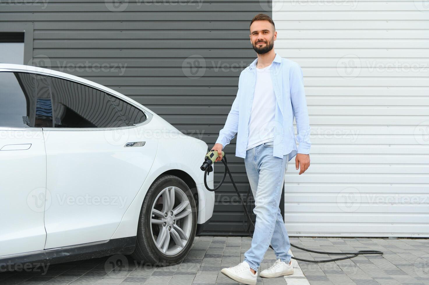 homme en portant Puissance mise en charge câble pour électrique voiture dans Extérieur voiture parc. et il s Aller à relier le voiture à le mise en charge station dans le parking lot près le achats centre. photo