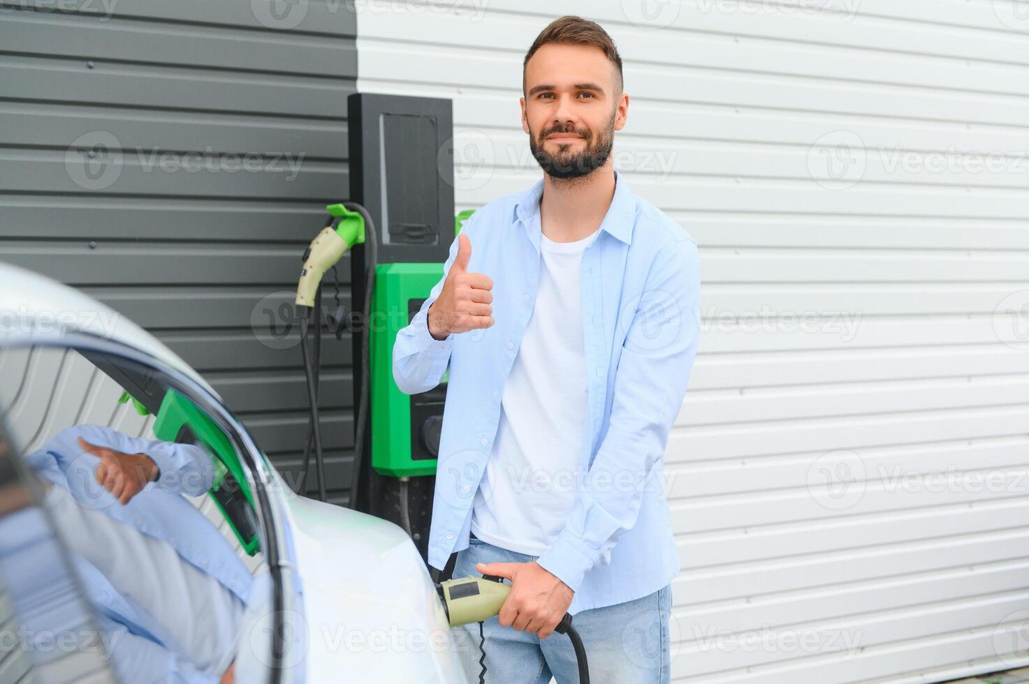 homme en portant Puissance mise en charge câble pour électrique voiture dans Extérieur voiture parc. et il s Aller à relier le voiture à le mise en charge station dans le parking lot près le achats centre. photo