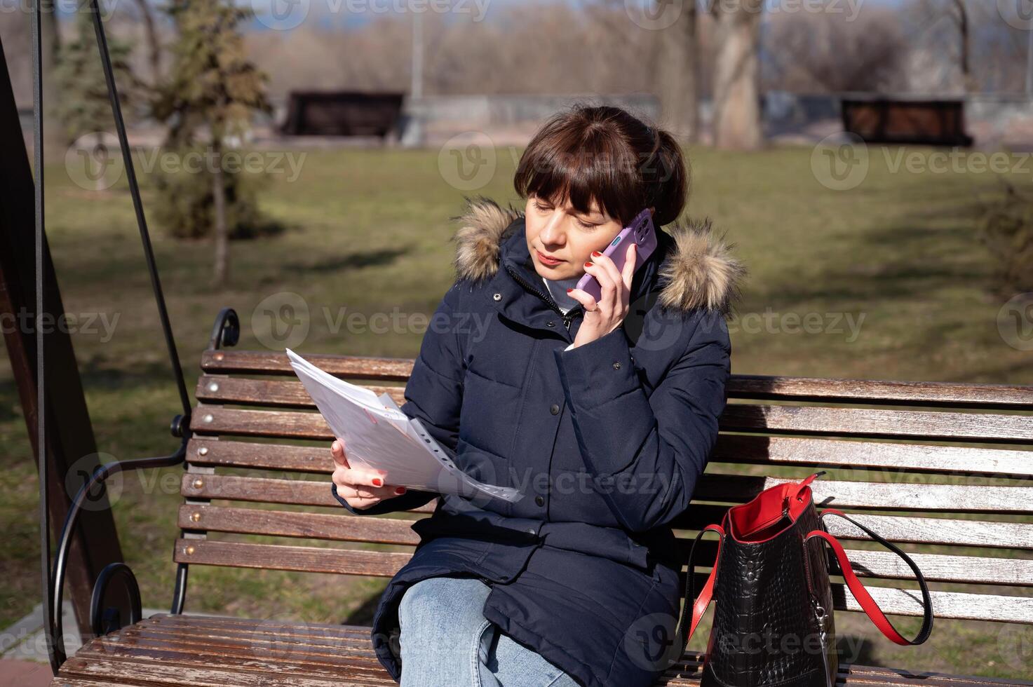 une Jeune femme comptable est assis sur une parc banc et lit une rapports document et appels sur une téléphone intelligent, rapports période photo