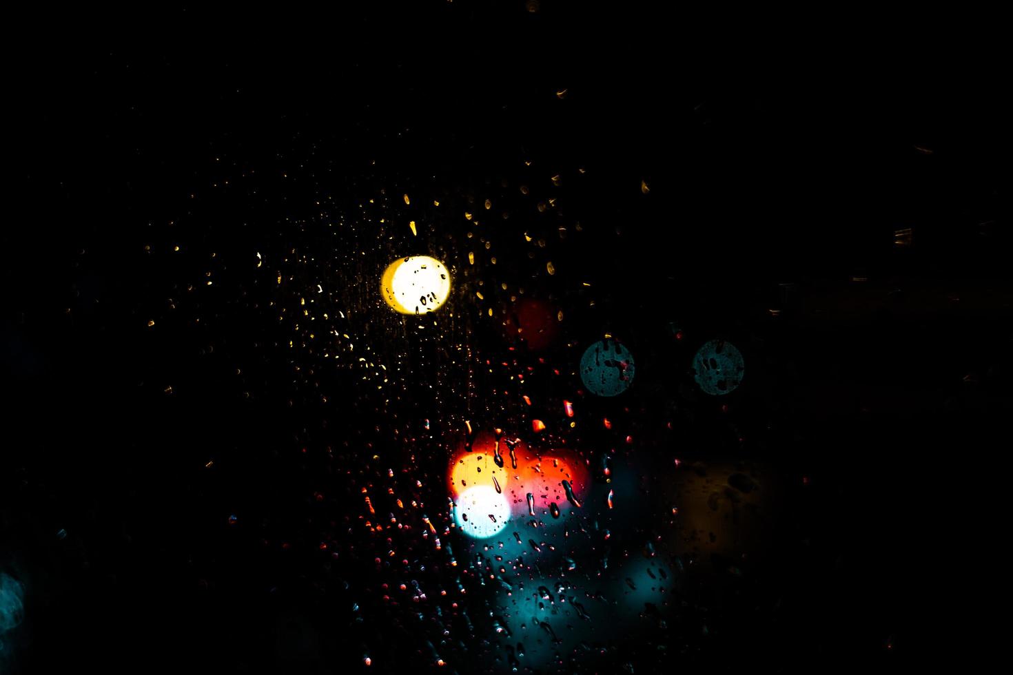 points de bokeh rouge bleu et jaune sur fond sombre qui viennent de derrière une voiture légère pendant la pluie et les embouteillages. photo