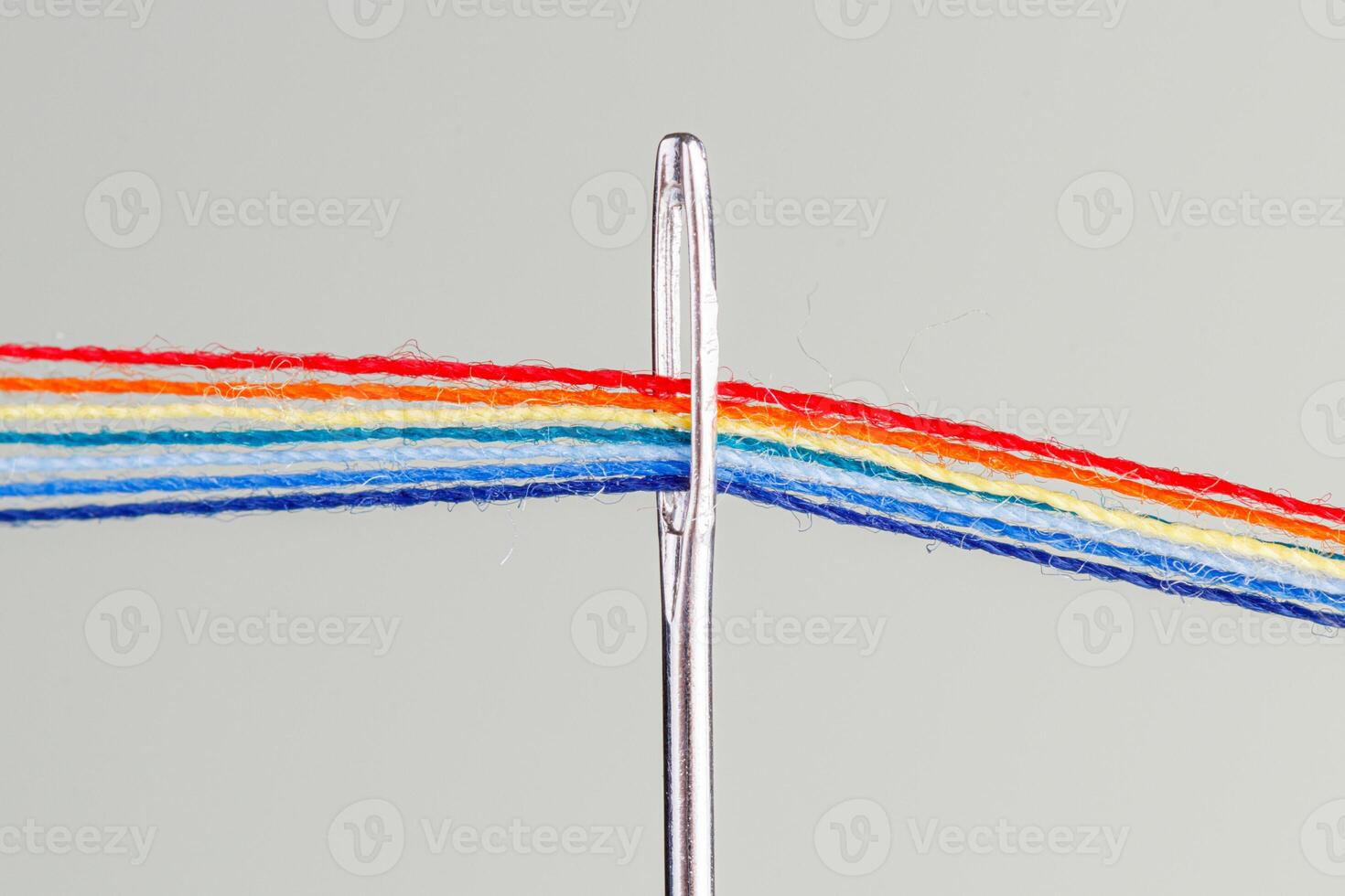 multicolore fils pour couture dans le forme de une arc en ciel passer par un antique aiguille sur une blanc Contexte photo