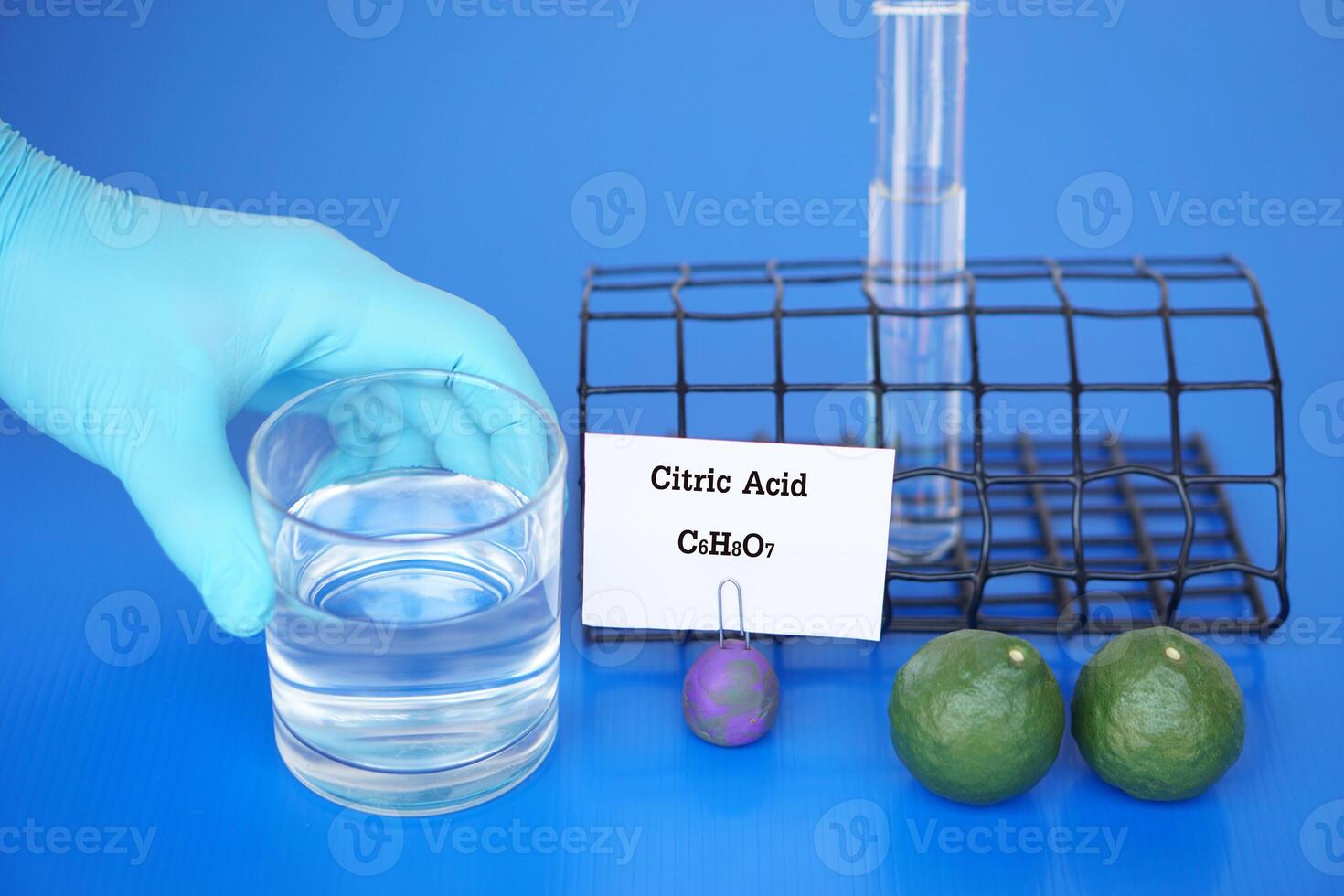 science expérience à propos citrique acide avec moléculaire formule c6h8o7. main dans bleu gant tenir verre de eau, tester tube et citron vert des fruits. concept, éducation, science laboratoire leçon. photo