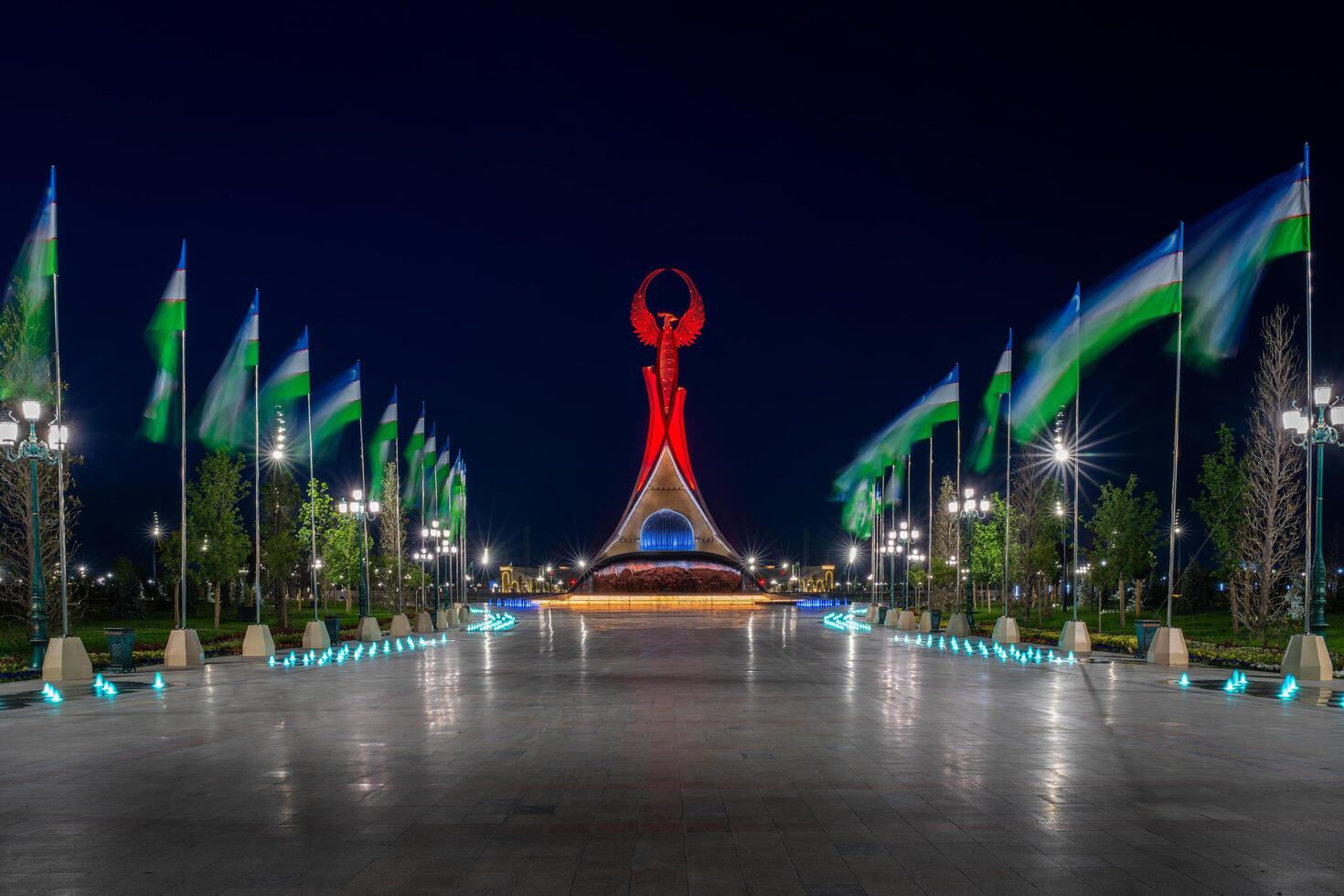 Ouzbékistan, Tachkent - mai 5, 2023 illuminé monument de indépendance dans le forme de une stèle avec une humo oiseau, fontaines et agitant drapeaux dans le Nouveau Ouzbékistan parc à la nuit. photo