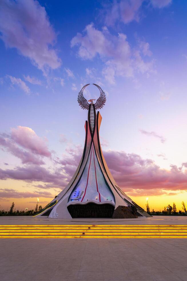 Ouzbékistan, Tachkent - octobre 4, 2023 monument de indépendance dans le forme de une stèle avec une humo oiseau sur une crépuscule avec Cliody ciel dans le Nouveau Ouzbékistan parc. photo