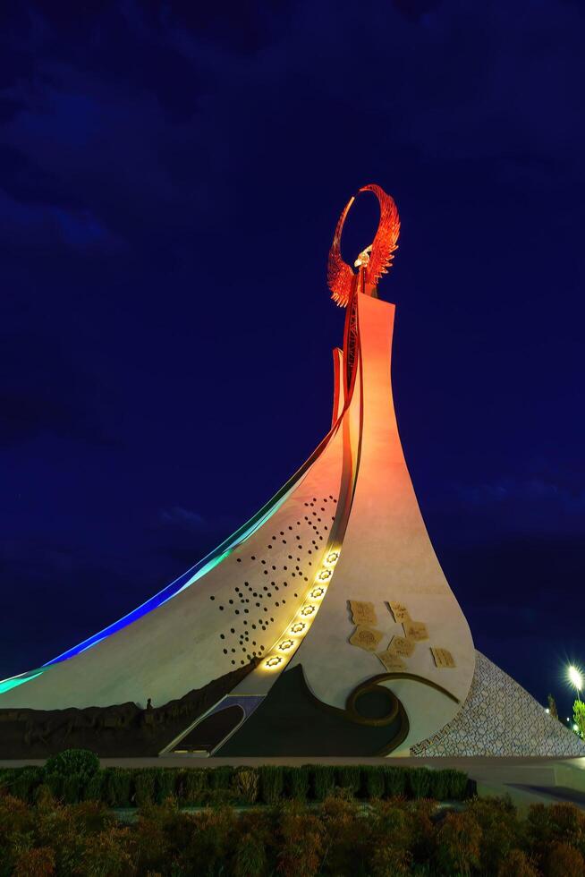 Ouzbékistan, Tachkent - octobre 4, 2023 illuminé monument de indépendance dans le forme de une stèle avec une humo oiseau dans le Nouveau Ouzbékistan parc à la nuit dans l'automne. photo