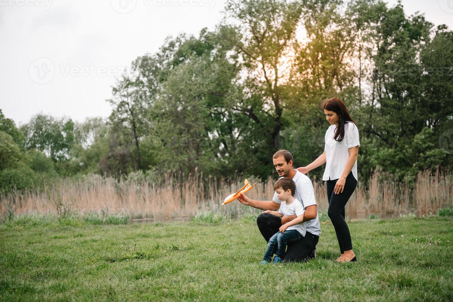 père, mère et fils en jouant avec jouet avion dans le parc. amical famille. gens ayant amusement en plein air. image fabriqué sur le Contexte de le parc et bleu ciel. concept de une content famille photo