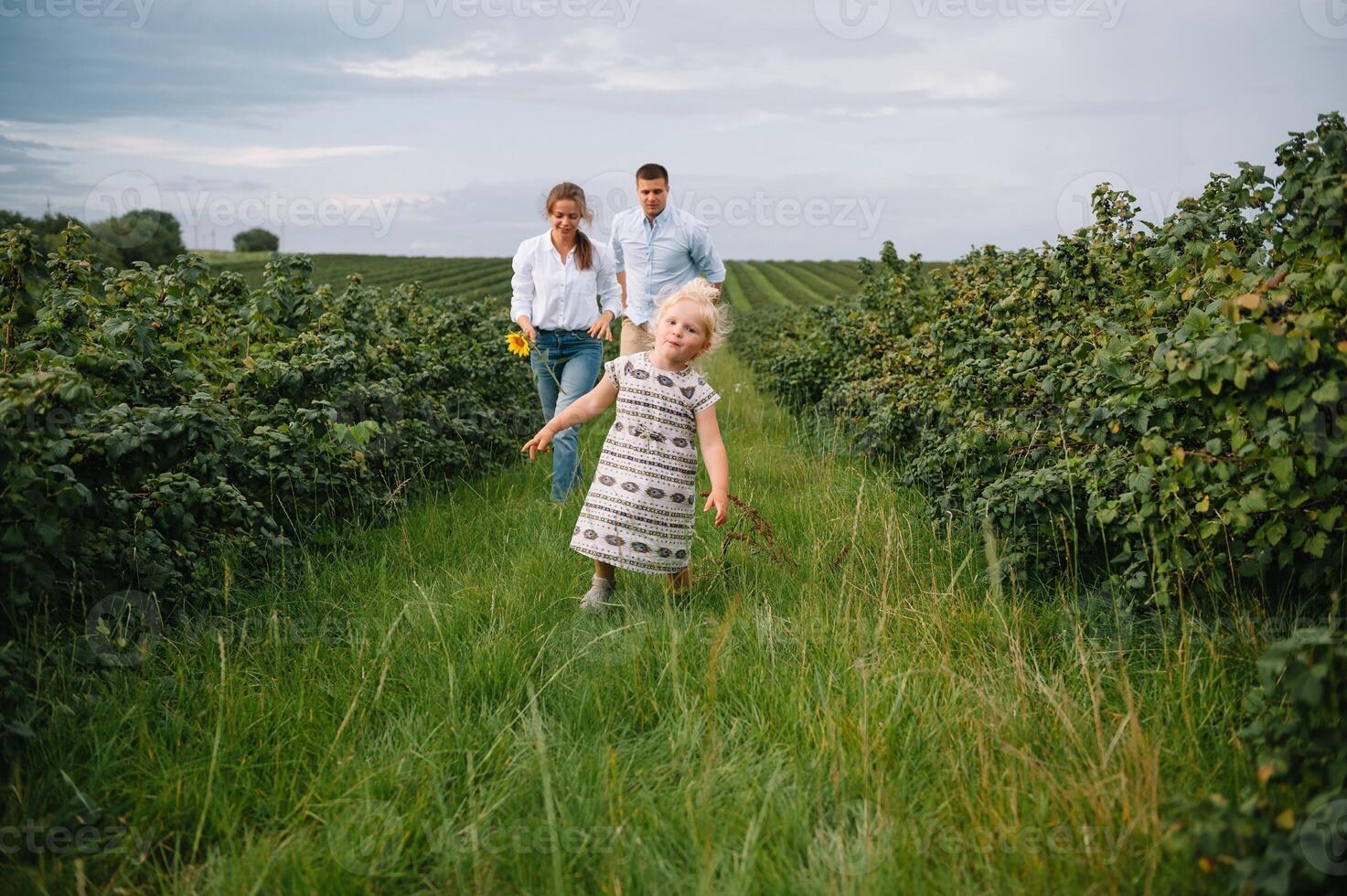 content famille en marchant dans le parc. maman, papa et fille marcher en plein air, Parents en portant le bébé les filles mains. enfance, la parentalité, famille obligations, mariage concept. photo